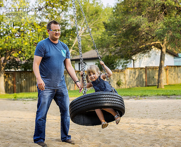 Ein Vater schiebt seine Tochter auf einer Reifenschaukel auf einem Spielplatz; Edmonton  Alberta  Kanada