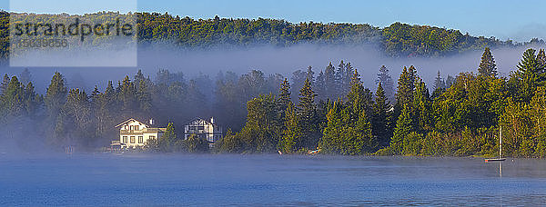 Nebel liegt über dem Lac a la Truite in der Morgendämmerung mit tief hängenden Wolken über dem Wald entlang des Ufers; Quebec  Kanada