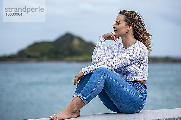 Porträt einer jungen Frau  die an einer Mauer am Meer sitzt; Wellington  Nordinsel  Neuseeland