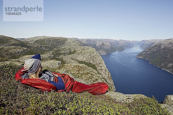Junge Frau im roten Schlafsack mit Blick auf den Fjord  Outdoor  Camping  Preikestolen  Rogaland  Norwegen  Europa