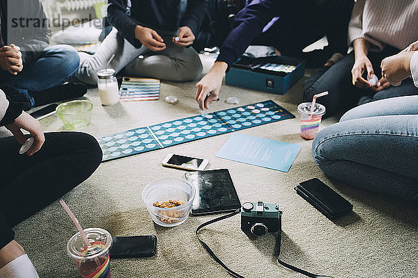 Niedriger Anteil von Freunden  die Brettspiele spielen  während sie zu Hause auf dem Boden Snacks essen