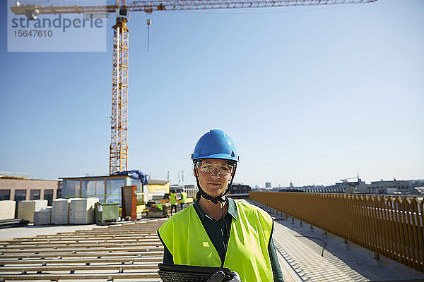 Selbstbewusste Ingenieurin in reflektierender Kleidung mit digitalem Tablet auf der Baustelle vor klarem Himmel