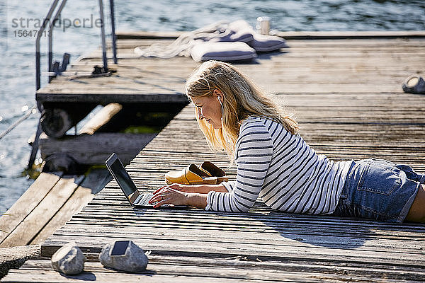 Mittelgroße Erwachsene  die während der Sommerferien über dem Holzsteg liegend am Laptop tippen