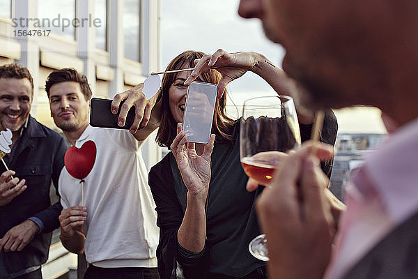 Geschäftskollegen machen Erinnerungen beim Fotografieren mit Smartphones bei Feierlichkeiten nach der Arbeit auf der Terrasse