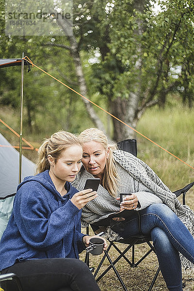Mutter und Tochter beim Kaffeetrinken auf dem Campingplatz vor einem Smartphone