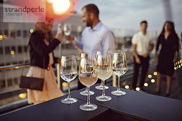 Nahaufnahme von auf dem Tisch arrangierten Weingläsern mit Geschäftsleuten im Hintergrund auf der Terrasse während der Party