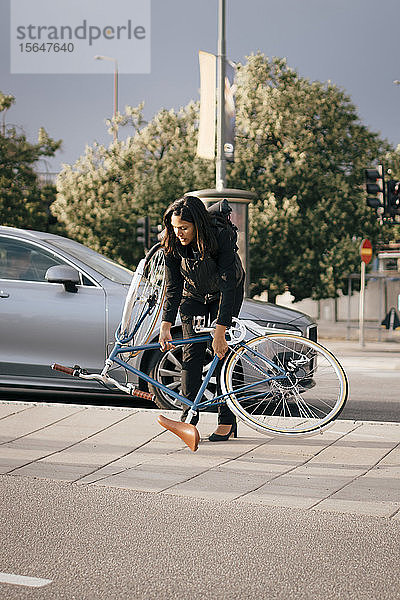 Geschäftsfrau hält Fahrrad beim Überqueren einer Straße in der Stadt