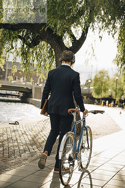 Rückansicht eines Geschäftsmannes zu Fuß mit dem Fahrrad auf einem Fußweg in der Stadt