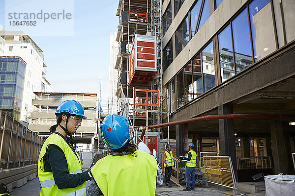 Architektinnen in reflektierender Kleidung diskutieren auf der Baustelle