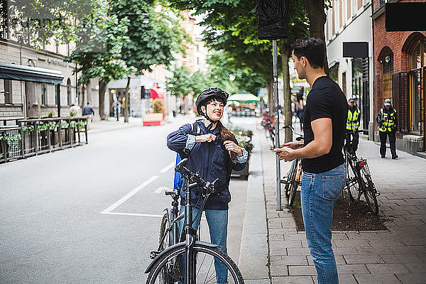 Lieferfrau im Gespräch mit einem männlichen Kunden  der in der Stadt auf dem Bürgersteig steht