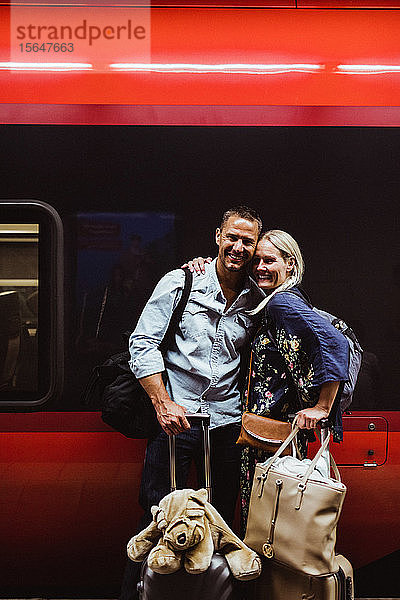 Porträt eines glücklichen Paares mit Gepäck  das am Bahnhof gegen den Zug steht
