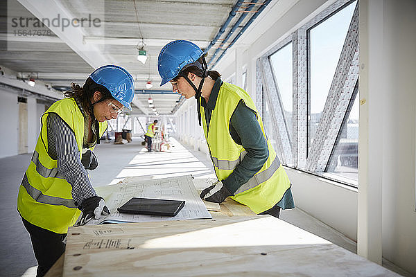 Seitenansicht von Ingenieurinnen  die auf der Baustelle über den Bauplan diskutieren