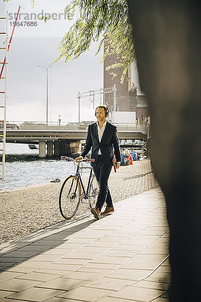 Geschäftsmann geht bei Sonnenschein mit dem Fahrrad auf einem Fußweg in der Stadt