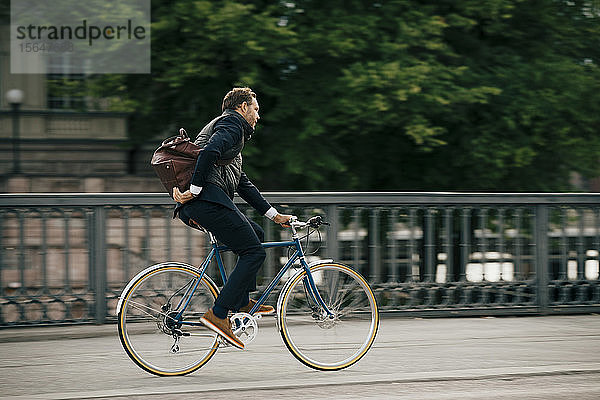 Seitenansicht eines Geschäftsmannes mit Tasche beim Fahrradfahren auf der Brücke