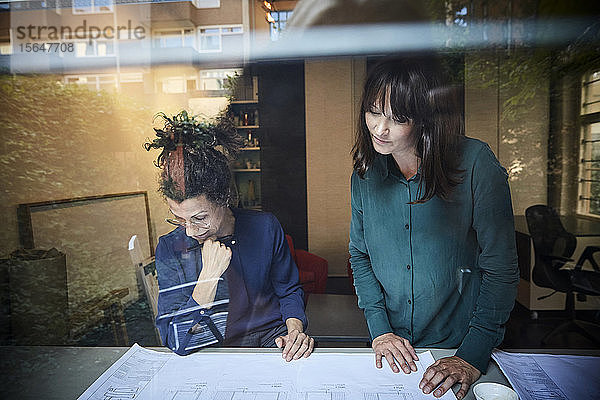 Architektinnen diskutieren über Blaupause am Tisch durch Glas gesehen im Büro