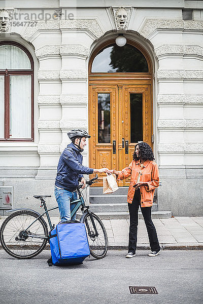 Lebensmittellieferant übergibt Paket an Frau  die in der Stadt auf dem Bürgersteig steht
