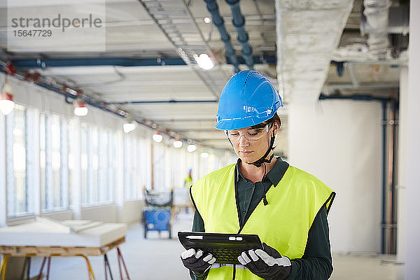 Selbstbewusste Ingenieurin in reflektierender Kleidung mit digitalem Tablett auf der Baustelle