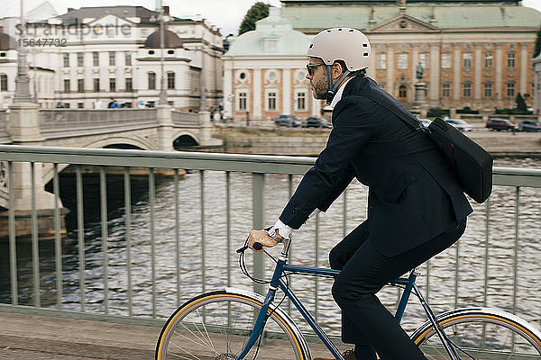 Seitenansicht eines Geschäftsmannes mit dem Fahrrad auf einer Brücke am Kanal in der Stadt