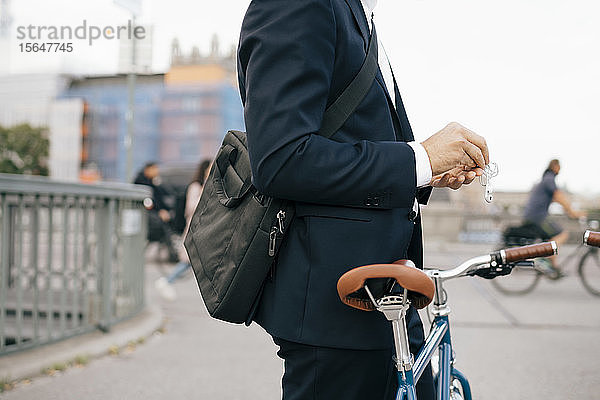 Geschäftsmann mit In-Ohr-Kopfhörern im Stehen mit Fahrrad auf einer Brücke in der Stadt