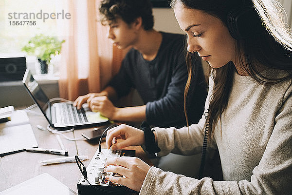Teenagerin beim Einstellen des Tonmischers  während sie mit einem Freund zu Hause am Laptop sitzt