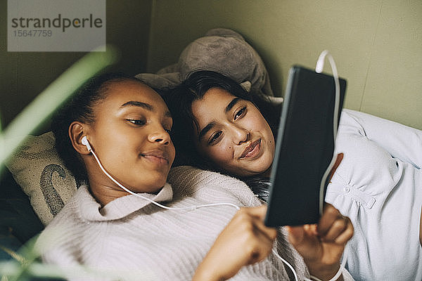 Weibliche Teenager  die zu Hause im Bett liegend Musik auf einem digitalen Tablet hören