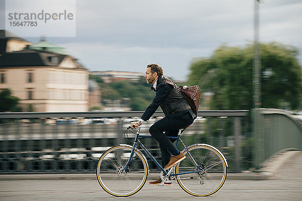 Selbstbewusster Geschäftsmann in voller Länge mit dem Fahrrad auf der Brücke