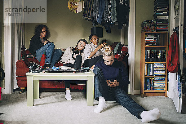 Abgelenkte Freunde benutzen Smartphones  während sie zu Hause zusammen sitzen