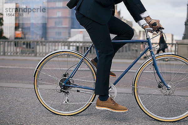 Niedriger Abschnitt eines Geschäftsmannes  der auf der Straße in der Stadt Fahrrad fährt