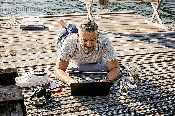 Reifer Mann liegt vorne  während er seinen Laptop über den Holzsteg benutzt