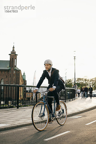 Zuversichtlicher Geschäftsmann fährt Fahrrad auf der Straße in der Stadt bei klarem Himmel