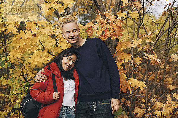 Lächelnde Teenager-Freunde stehen im Herbst an Ahornbäumen