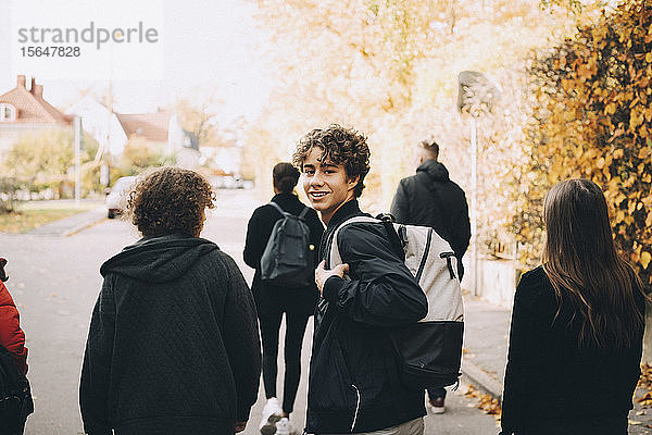 Porträt eines lächelnden Teenagers mit Rucksack beim Spaziergang mit Freunden auf der Straße in der Stadt