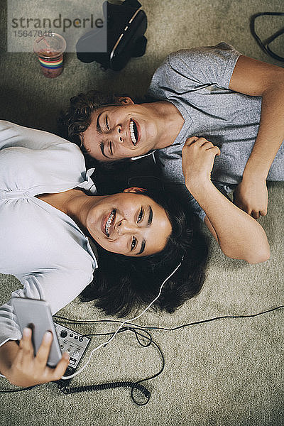 Direkt über der Aufnahme von glücklichen Freunden  die zusammen Musik hören  während sie zu Hause auf dem Teppich liegen
