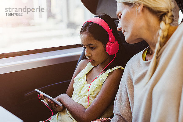 Mutter schaut Tochter an  die während einer Zugfahrt auf einem Smartphone einen Film ansieht