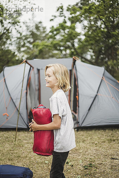 Seitenansicht eines lächelnden Jungen  der das Zelt hält  während er gegen das Zelt steht