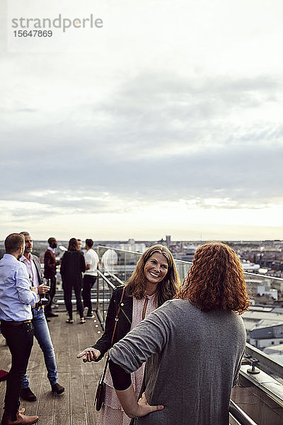 Lächelnde Geschäftsleute diskutieren während der Büroparty auf der Terrasse