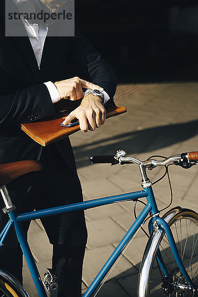 Mittelteil eines Geschäftsmannes  der die Zeit überprüft  während er mit dem Fahrrad auf einem Fußweg in der Stadt steht