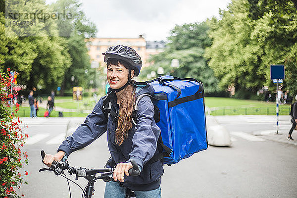 Porträt einer lächelnden Essenslieferantin mit Fahrrad auf der Straße in der Stadt