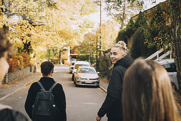 Porträt eines lächelnden Teenagers  der mit Freunden auf der Straße in der Stadt spazieren geht