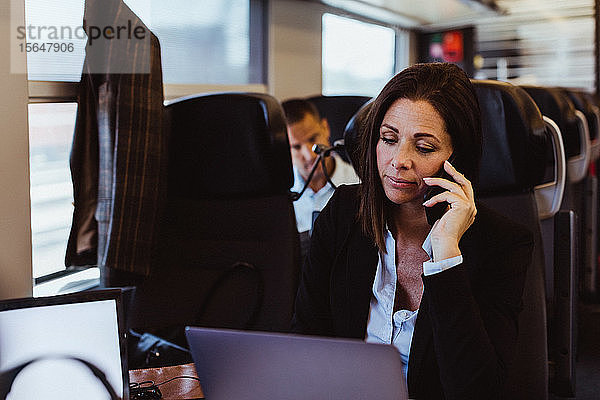 Geschäftsfrau spricht mit Smartphone und Laptop während der Fahrt im Zug