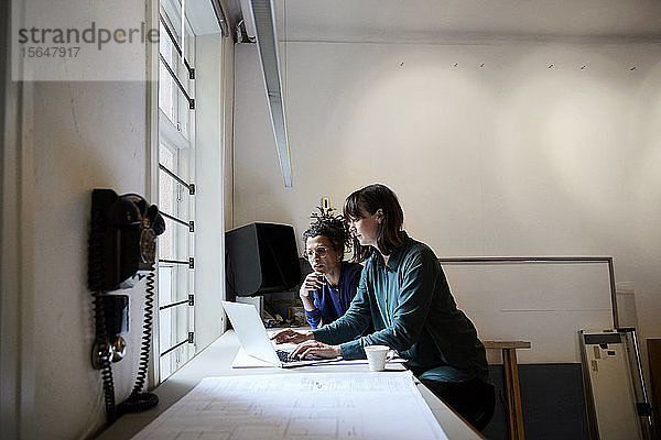 Architektinnen diskutieren am Laptop bei Tisch im Büro