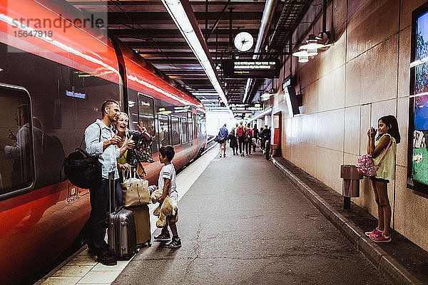 Mädchen fotografiert Familie  die mit Gepäck am Bahnhof gegen den Zug steht