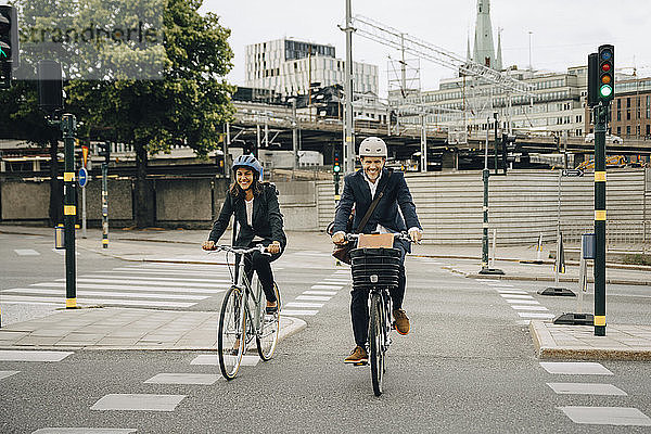Lächelnder Geschäftsmann und Geschäftsfrau fahren Fahrrad auf der Straße in der Stadt