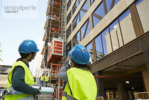 Ingenieurinnen in reflektierender Kleidung diskutieren auf der Baustelle