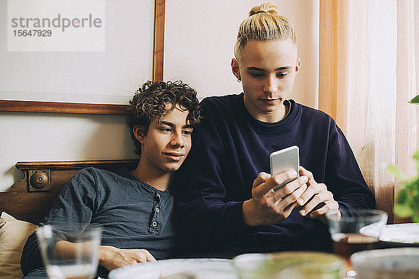 Jungen im Teenageralter  die zu Hause auf dem Sofa liegend ein Mobiltelefon benutzen