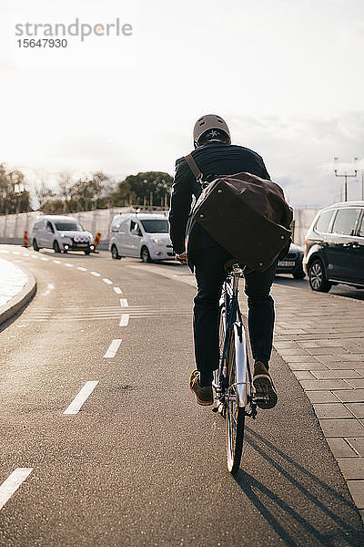 Rückansicht eines Geschäftsmannes  der an einem sonnigen Tag auf der Straße in der Stadt Fahrrad fährt