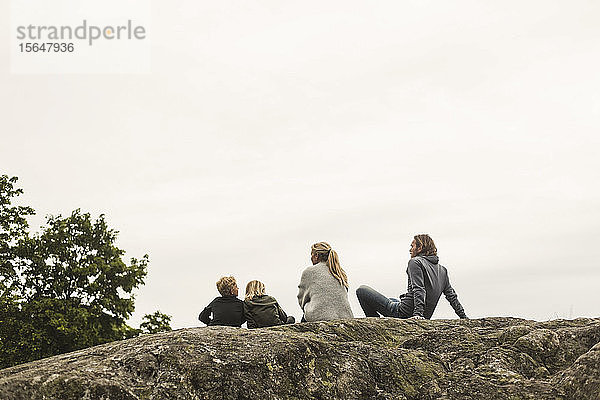 Familie ruht gemeinsam auf einer Felsformation vor klarem Himmel