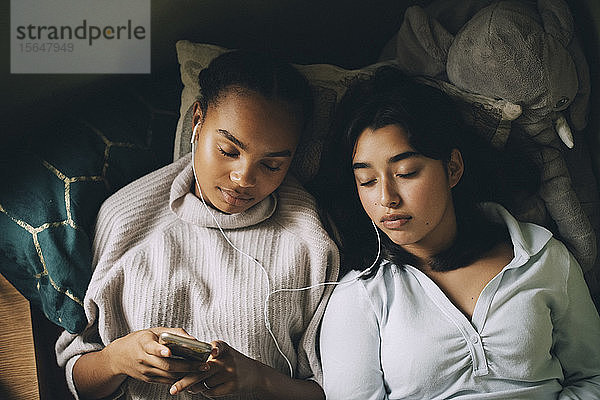 Mädchen im Teenageralter mit geschlossenen Augen  die zu Hause im Bett liegend über ein Smartphone Musik hören