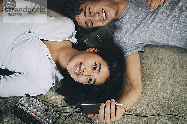 Fröhlicher Teenager  der sich mit seinem Freund am Mobiltelefon auf den Boden im Wohnzimmer legt