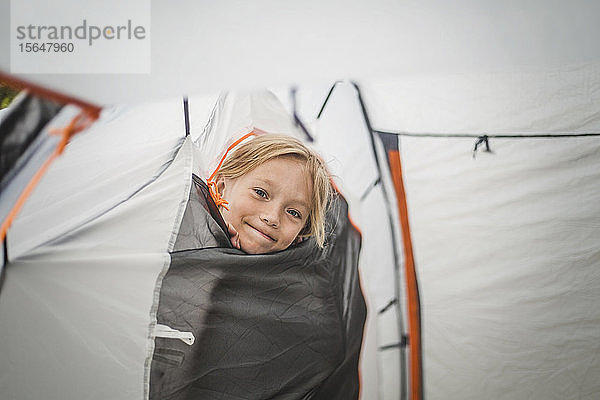 Porträt eines lächelnden Mädchens  das durch das Zelt auf dem Campingplatz schaut